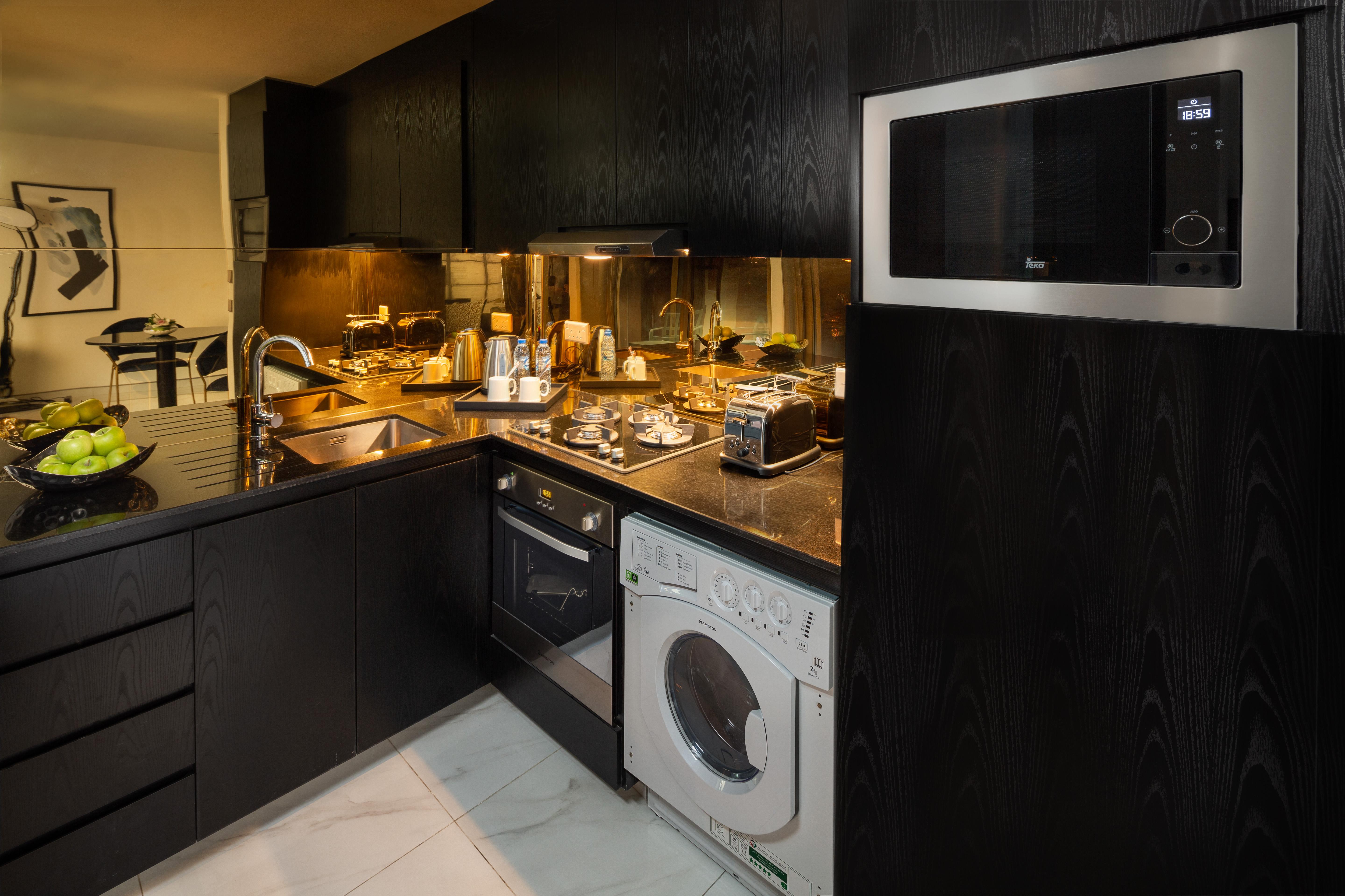 Aparthotel Millennium Atria Business Bay Dubai Exterior foto The photo shows a modern kitchen with a sleek design featuring black cabinetry and countertops. There is a sink with a faucet, a stove with multiple burners, and an oven integrated into the cabinetry. A microwave is mounted above the counter for conv