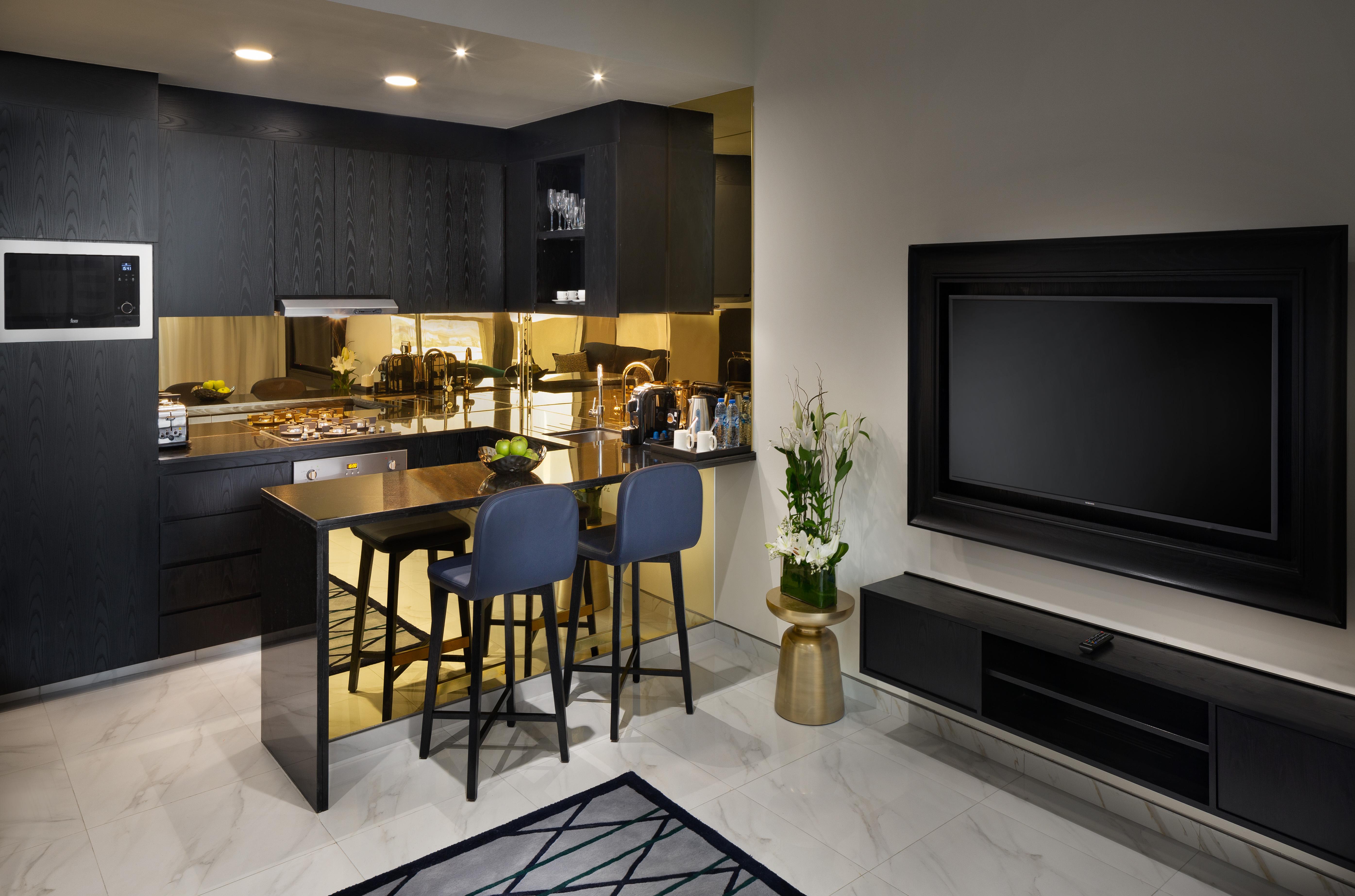 Aparthotel Millennium Atria Business Bay Dubai Exterior foto The photo depicts a modern kitchen and living area. The kitchen features dark cabinetry with a clean design, showcasing various appliances, including a stovetop and possibly an oven. There is a kitchen island with two stools, suggesting a space for c