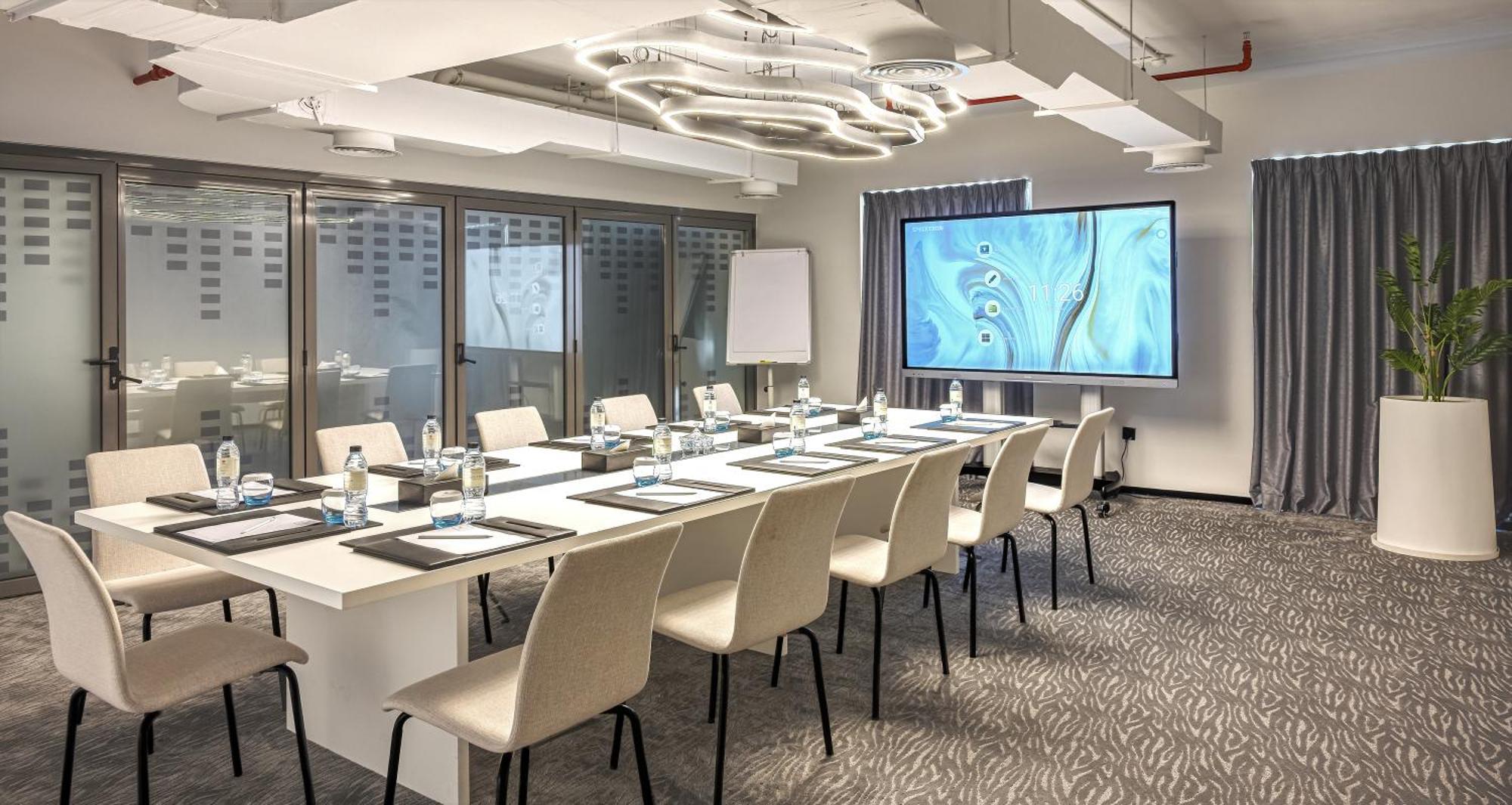 Aparthotel Millennium Atria Business Bay Dubai Exterior foto The photo shows a modern conference room set up for a meeting. There is a long table with several chairs arranged around it, each with a notepad and pen. A large screen displays a graphic or presentation, and there is a whiteboard in the corner. The 