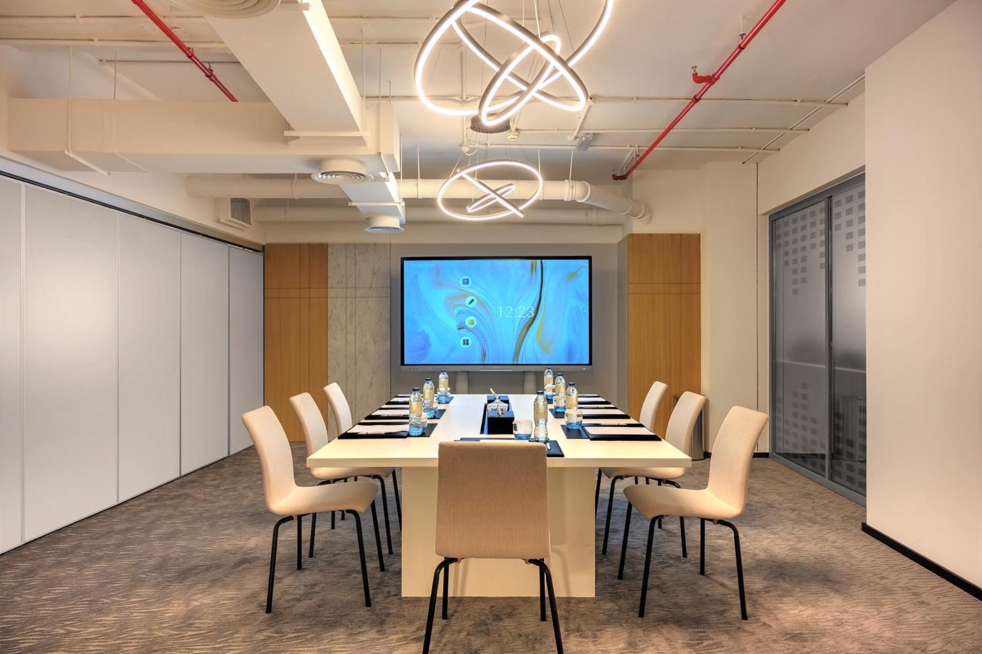 Aparthotel Millennium Atria Business Bay Dubai Exterior foto The photo shows a modern conference room designed for meetings. It features a long white table surrounded by beige chairs. At the end of the table, there is a large screen displaying a blue abstract design. The room is well-lit with contemporary ligh