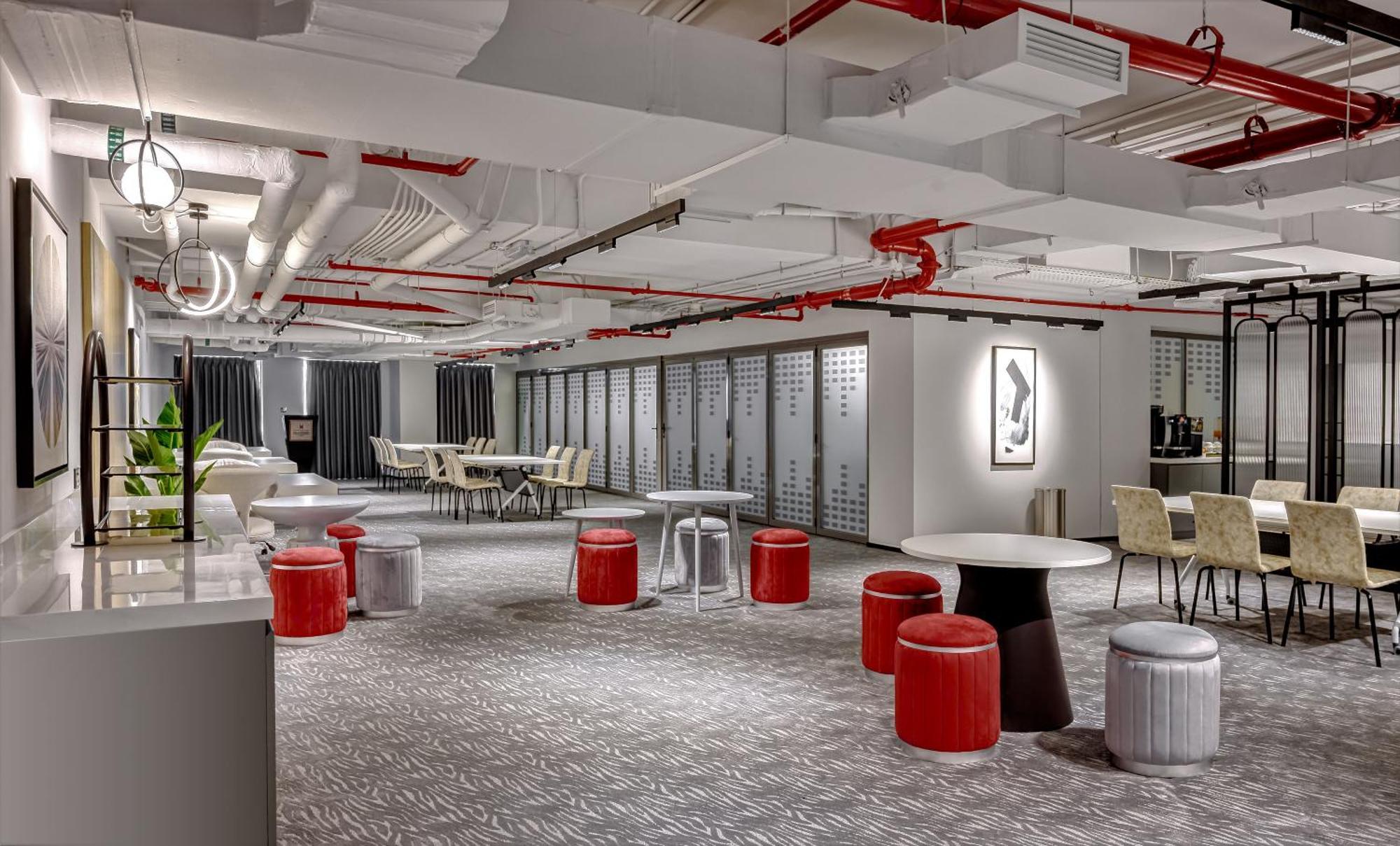 Aparthotel Millennium Atria Business Bay Dubai Exterior foto The photo shows a modern interior space, likely an office or communal area. The flooring is covered with a textured carpet, and the ceiling features exposed pipes painted red. 

There are several seating options, including small round tables with sto